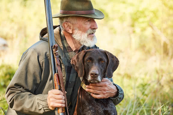 A man holding a rifle with an arm round his dog